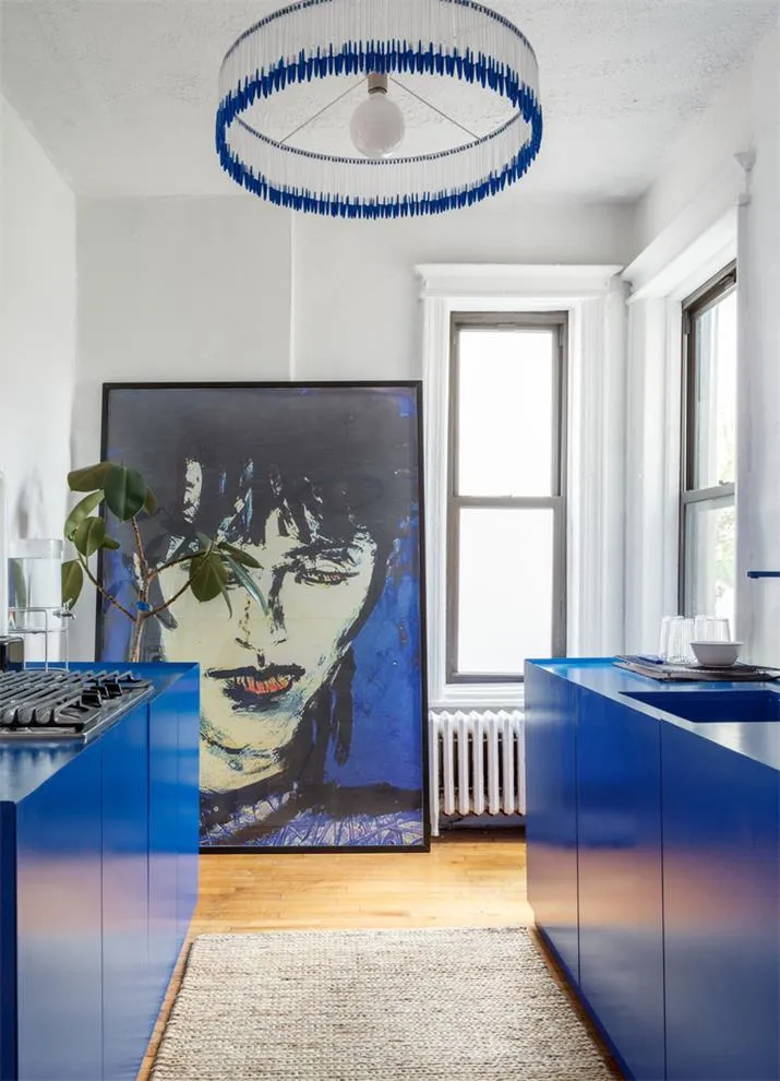 A modern kitchen with blue cabinets and a large window allowing natural light to flood the space. The ceiling features a uniq