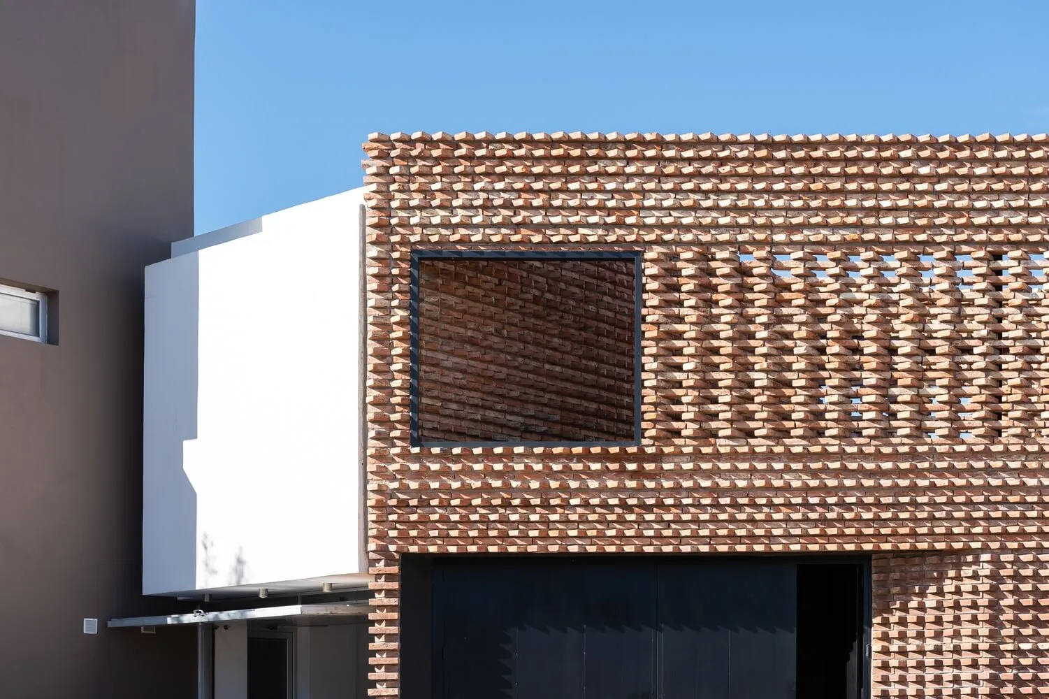 A modern building exterior featuring a brick facade with geometric patterns and a large window.