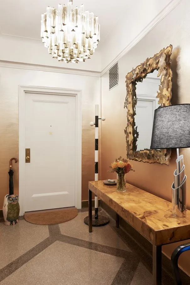 A modern entryway featuring a wooden bench, metal lamp, and vase of flowers.