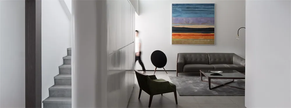 A modern living room featuring a concrete staircase, a sleek sofa upholstered in dark leather, and a contemporary art piece o