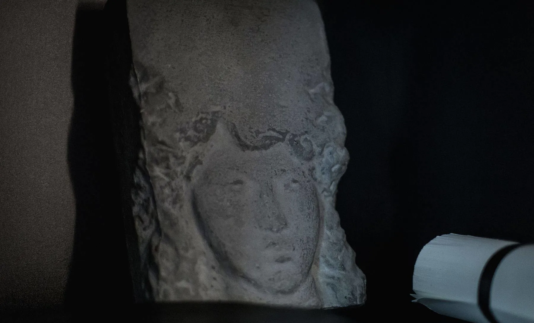 Detail of an ancient stone sculpture profile with a dark background and a light source on the right side.