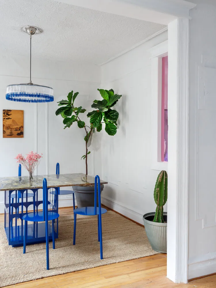 A minimalist dining room with a metallic dining table, blue chairs, and potted plants.