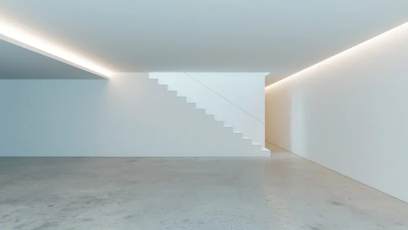 A minimalist interior with concrete walls, white walls, and a staircase leading to another level.