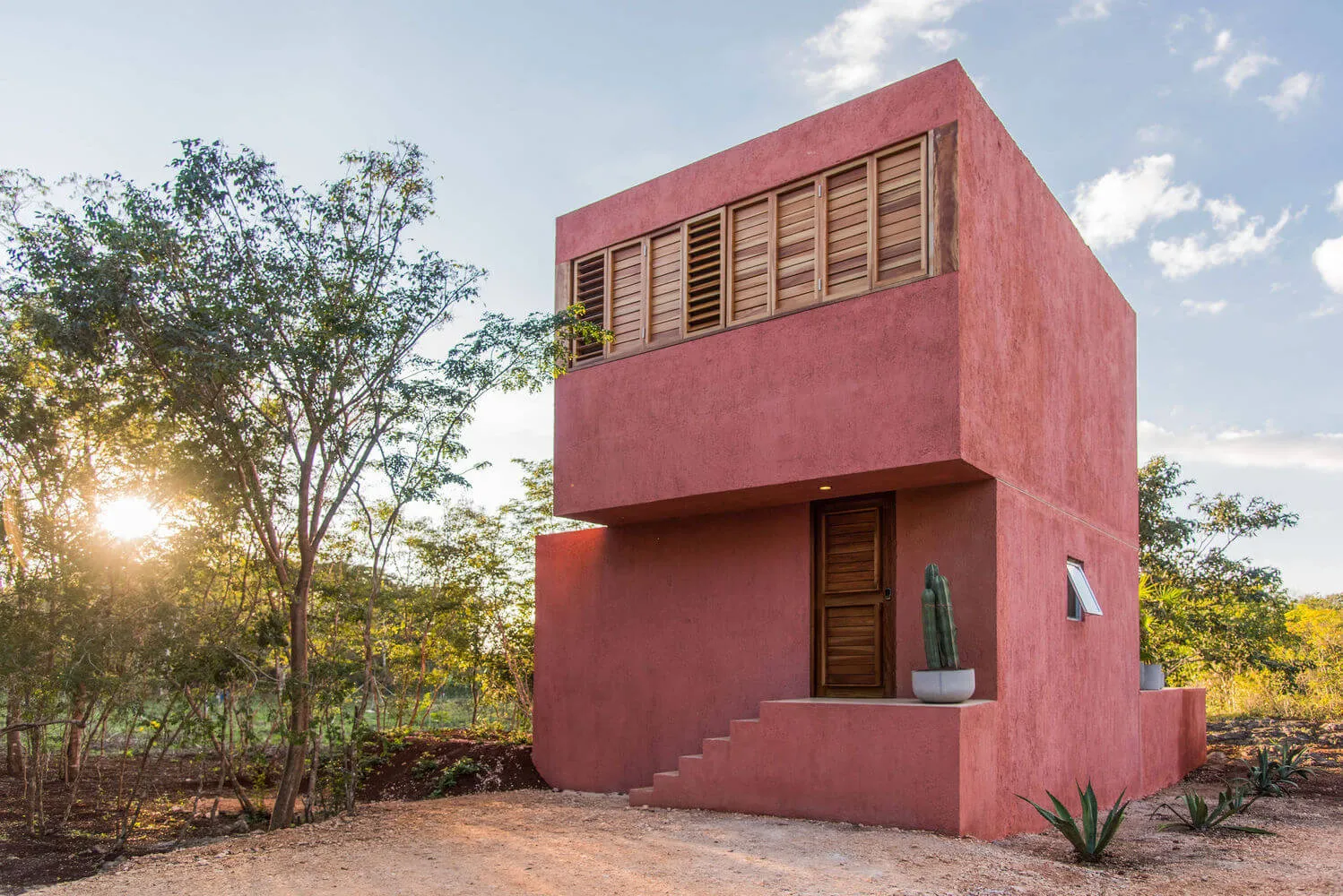 A modern, single-story house with concrete walls, wooden shutters, and a small cactus plant.