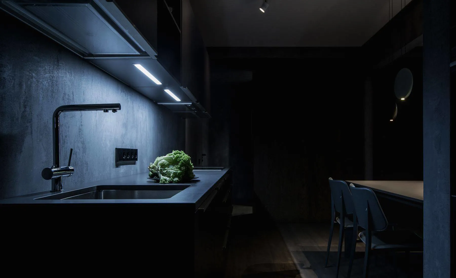 A modern, minimalist kitchen with black countertops and a concrete backsplash.