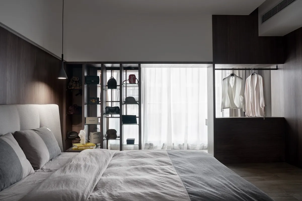 A modern bedroom featuring a bed with a neutral-colored bedspread and pillows, alongside shelves and dressers adorned with ba