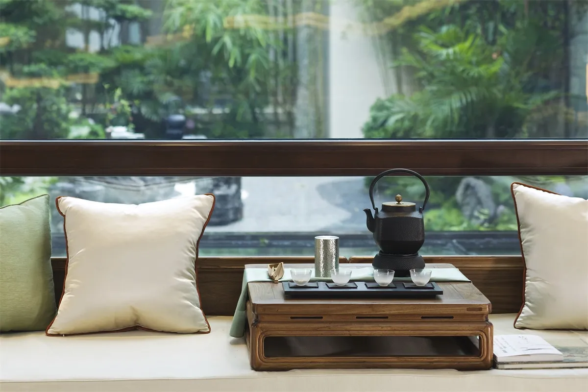 A modern living room featuring wooden furniture, green cushions, and a small table with a teapot and cups.
