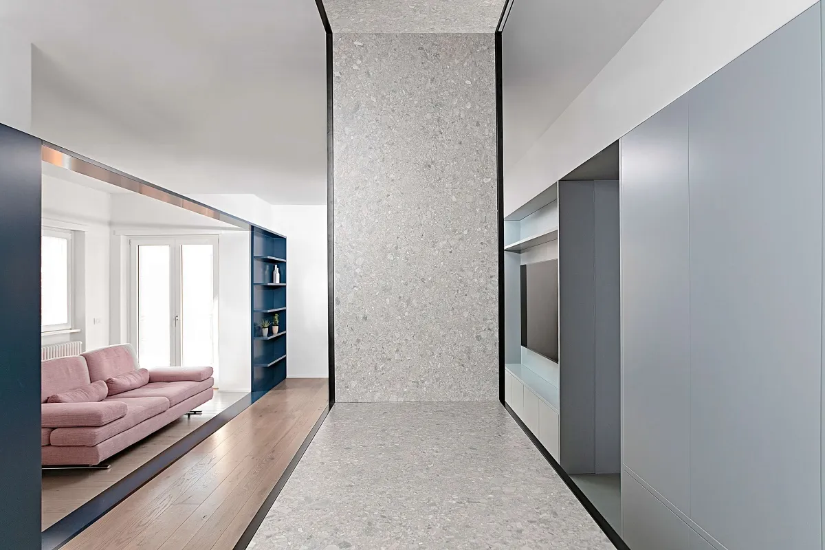 Modern minimalist living room featuring a pink sofa, blue shelving unit, and grey concrete walls.