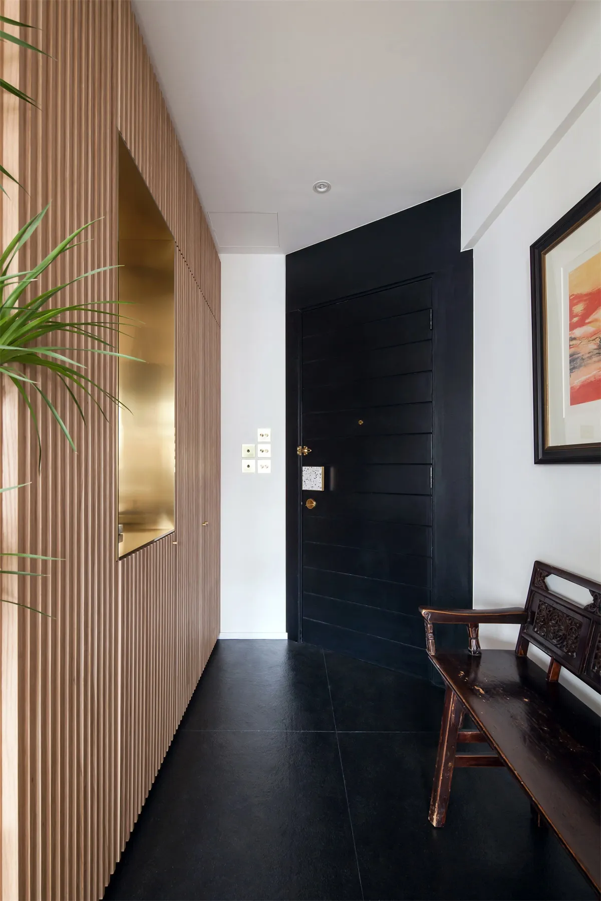 A modern entryway featuring black wooden walls and flooring, with a black door and wooden bench.