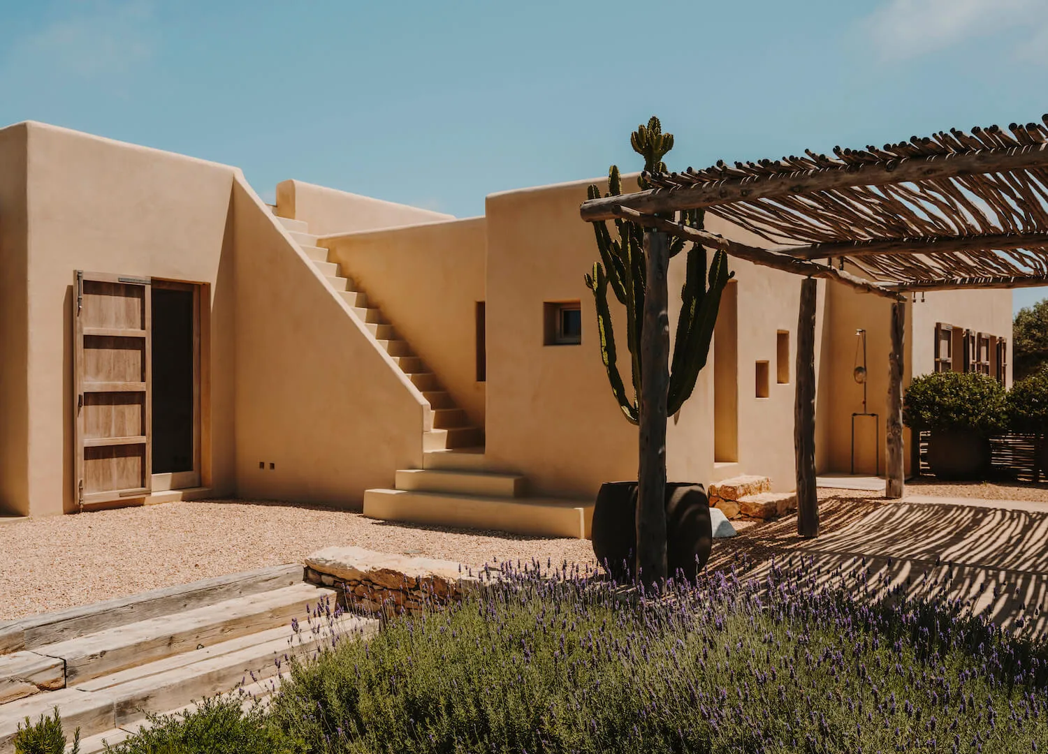 A modern house with sandstone walls, an outdoor staircase, and a pergola with cacti.