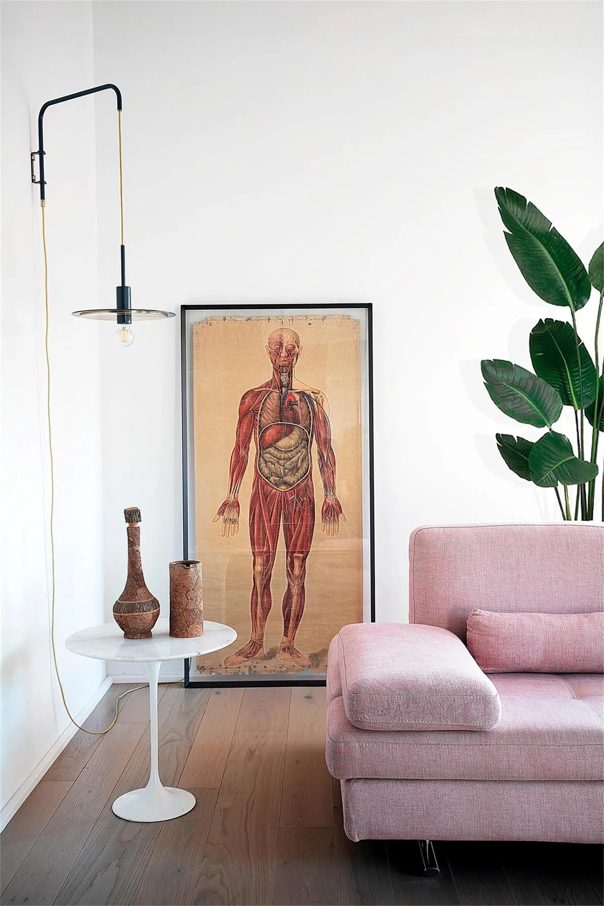 A modern minimalist living room with a pink sofa, wooden flooring, and a wall-mounted lamp.