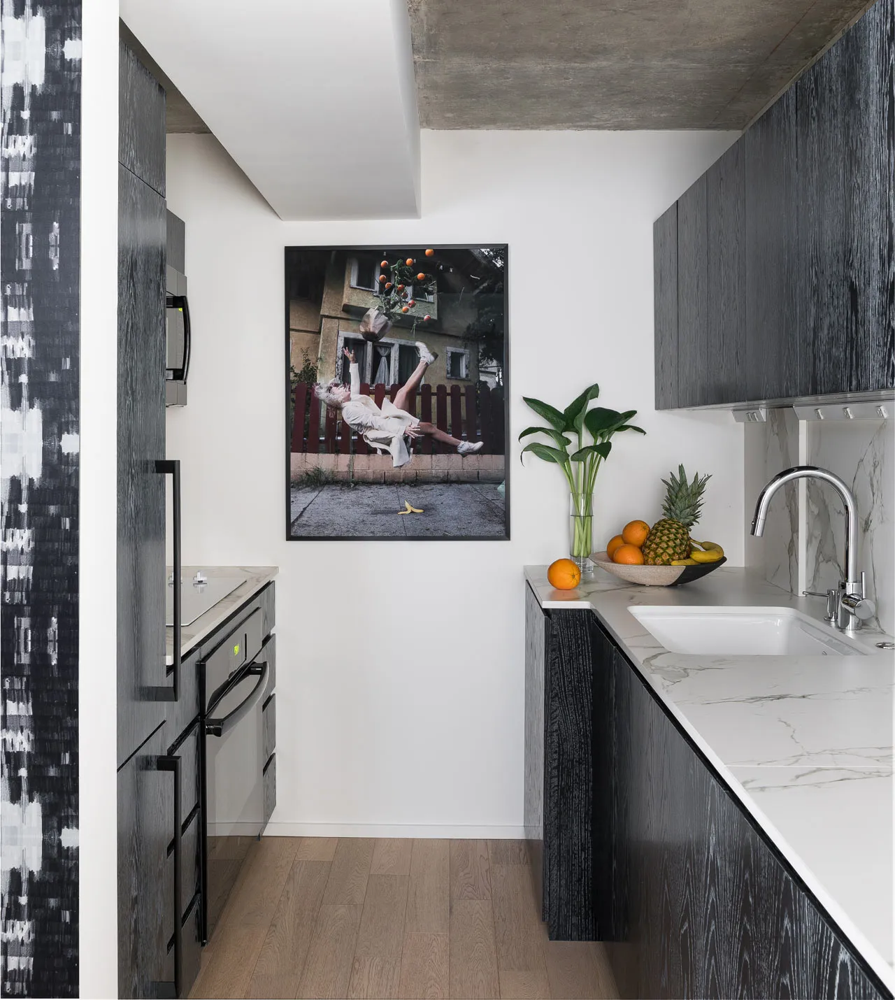 A modern minimalist kitchen with black-wood cabinetry and white-marble countertops, featuring a sink with fruits and a framed