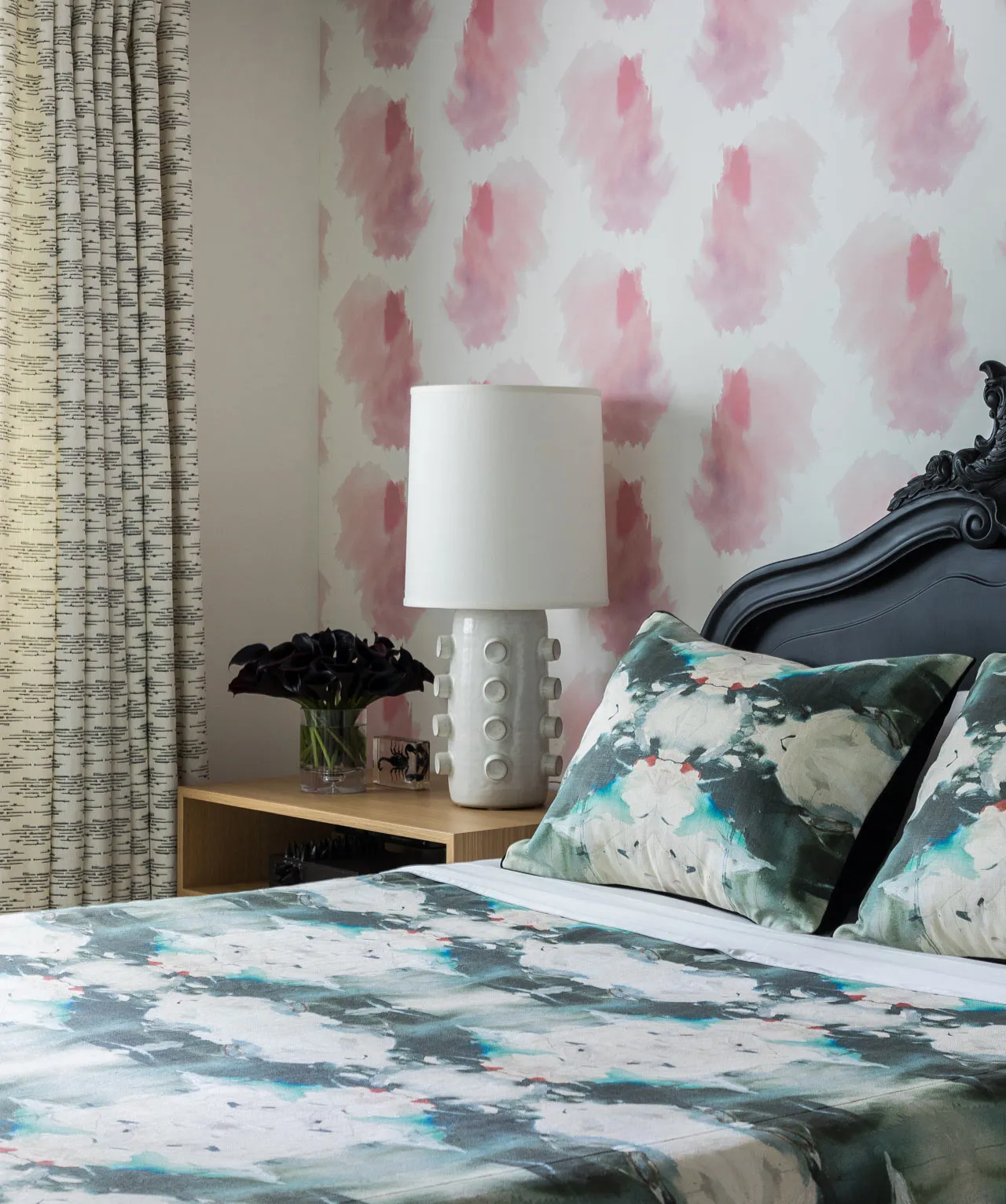 Modern bedroom with a patterned bedspread, floral pillows, and a white lamp on a wooden shelf.
