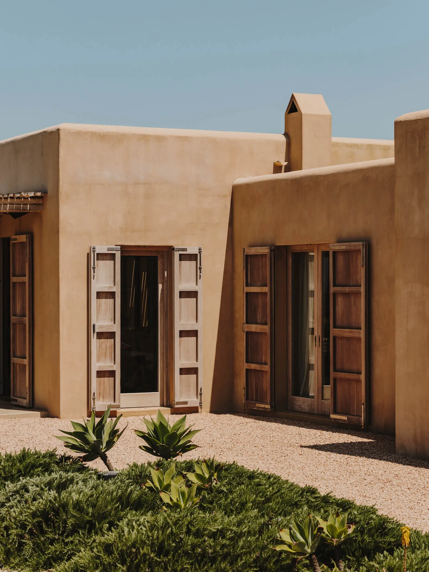 A modern building with earth-toned walls and large wooden doors and windows.