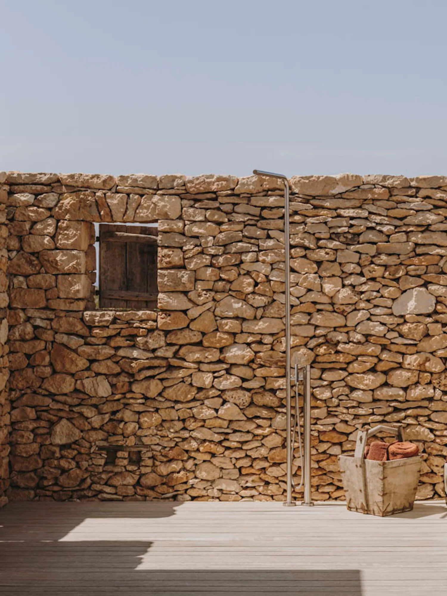 An outdoor shower with a stone wall and wooden floor.