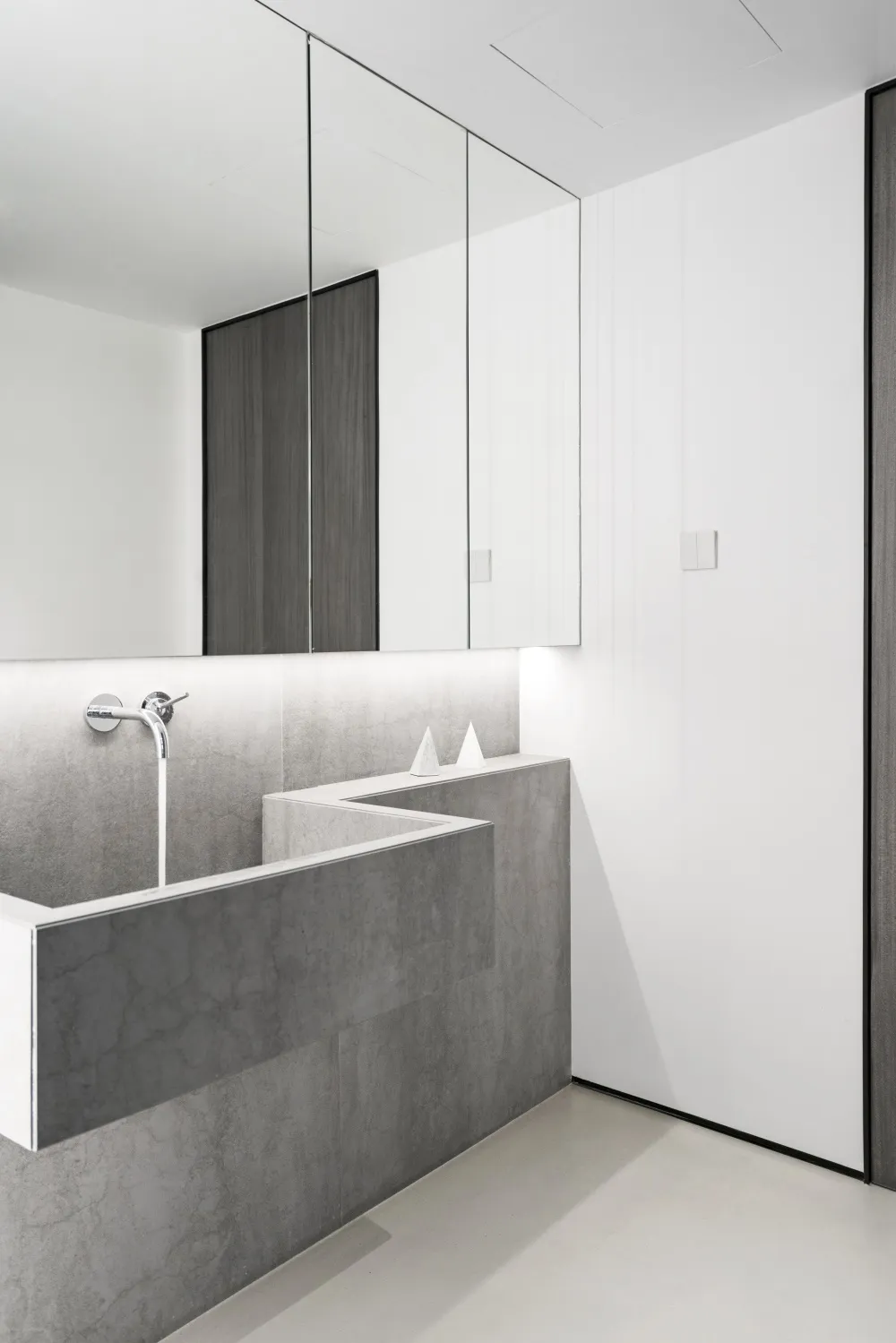 Modern minimalist bathroom with concrete trough sink and white wall cabinets.