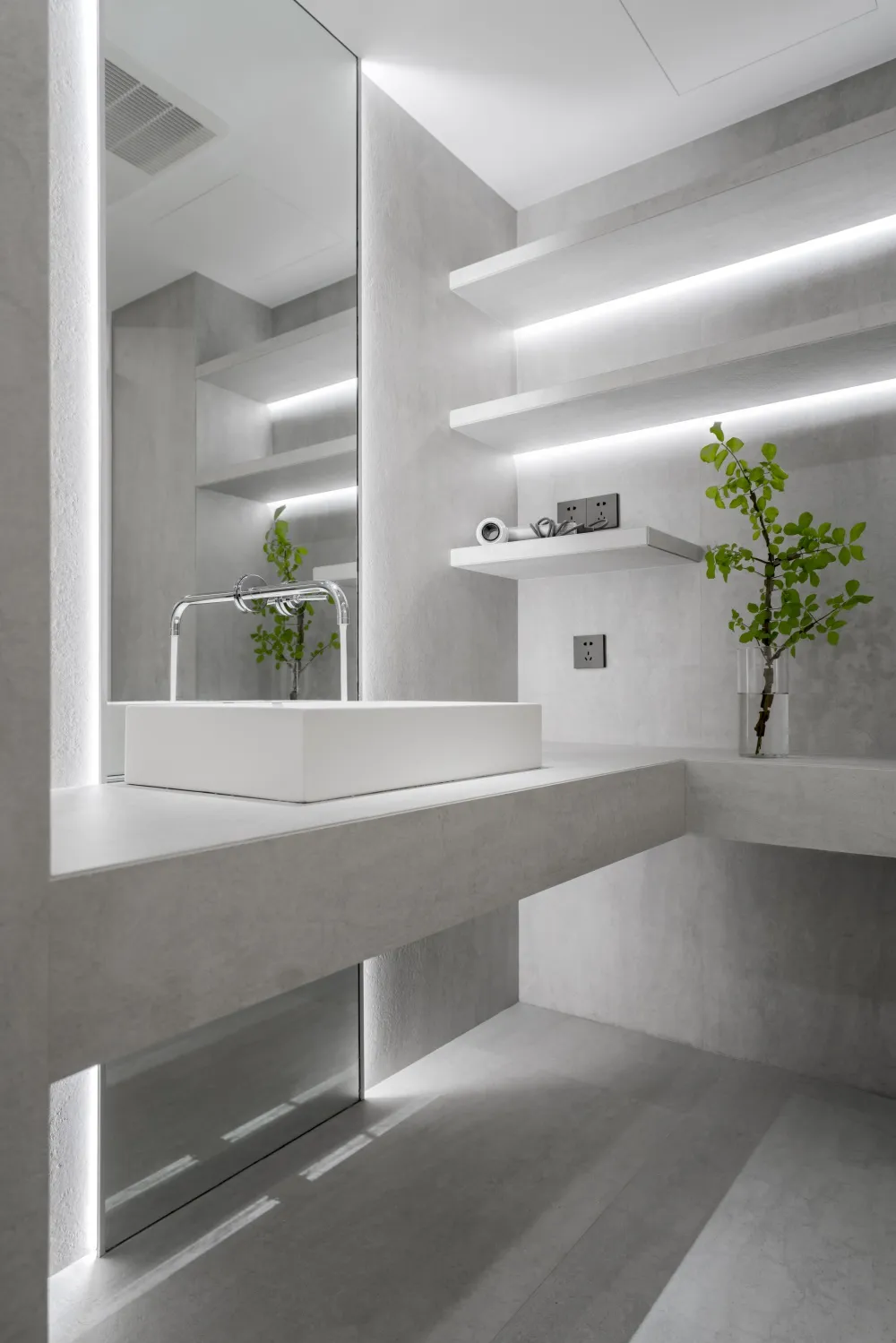 Minimalist modern bathroom with white concrete walls and floor, sleek white square sink, and floating white shelves with buil