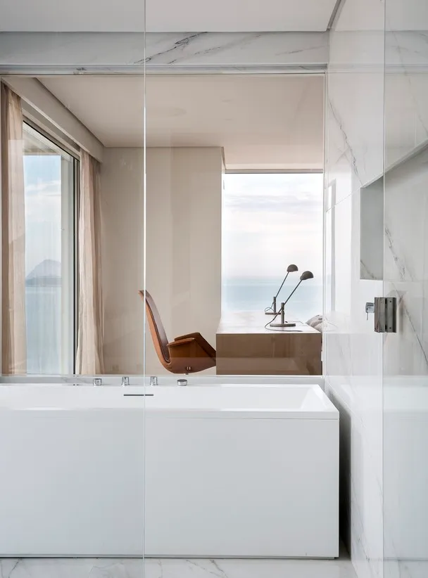 A minimalist bathroom featuring a white marble bathtub with an ocean view.