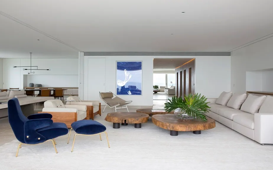 Modern living room with white furniture, wooden tables, blue chairs, and a large window.