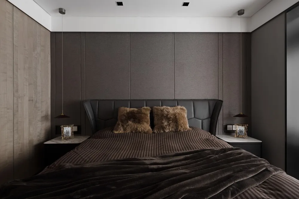 A modern minimalist bedroom featuring a bed with leather headboard and brown fabric bedding, alongside plush pillows and a co