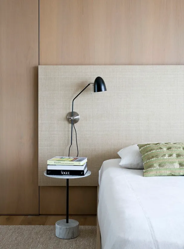 A minimalist bedroom with textured walls, a white bed, and a small side table with books and a lamp.