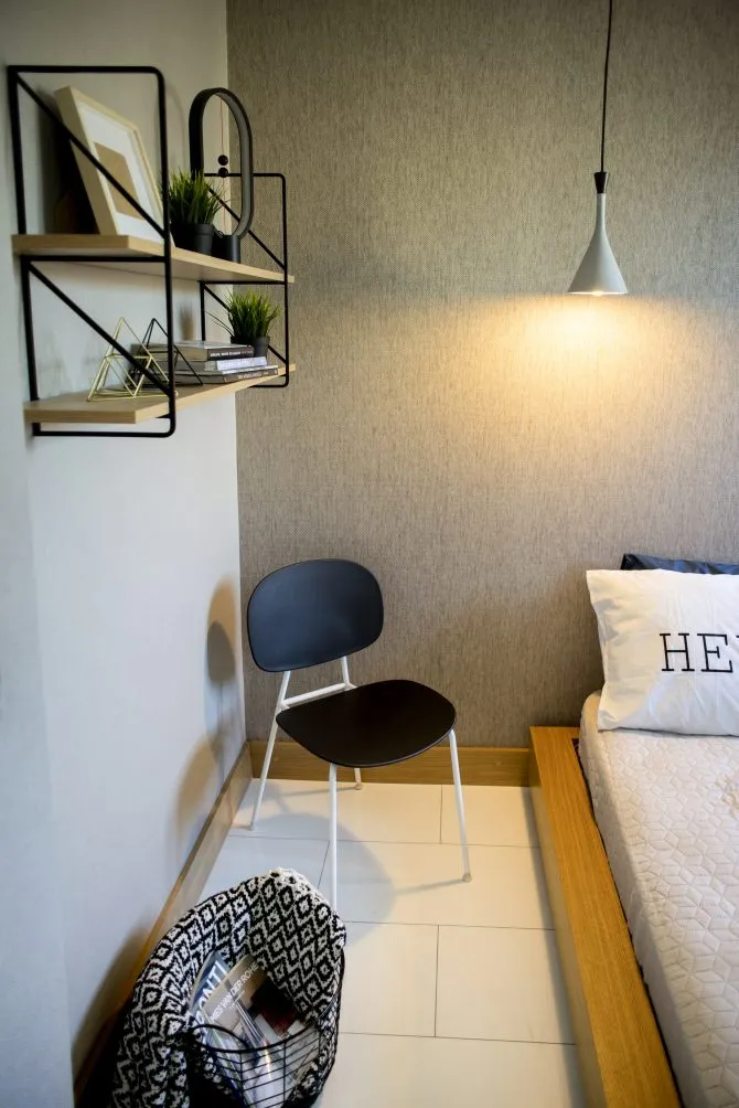 A minimalist bedroom with a bed, chair, shelves, and a hanging lamp.