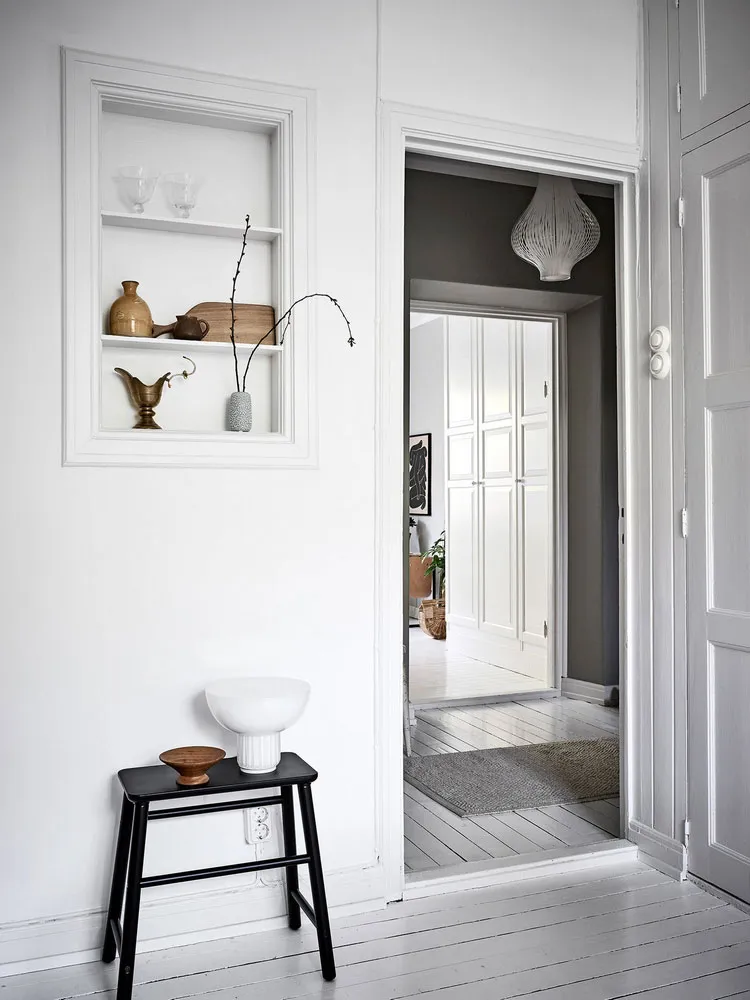 A minimalist interior design featuring a white space with wooden furniture and decorative objects on shelves.