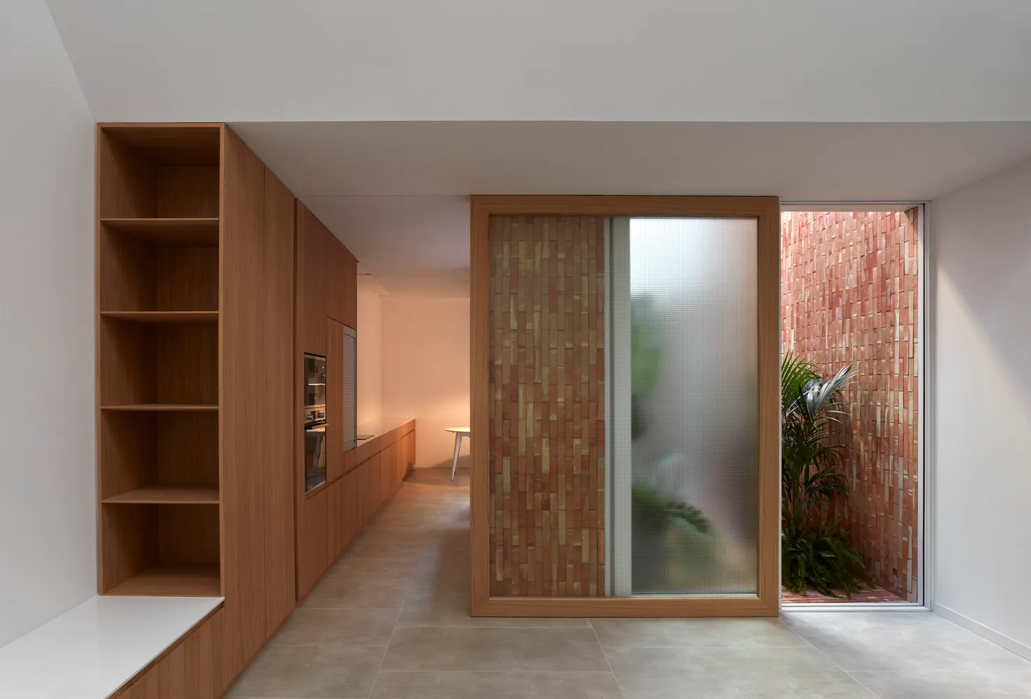 Modern minimalist residential interior with wooden cabinetry, glass sliding door, and greenery.