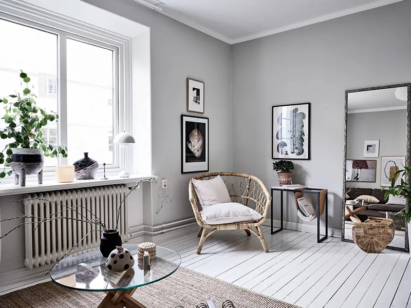 A modern minimalist living room with white walls, a wicker chair, a glass coffee table, and a large window.