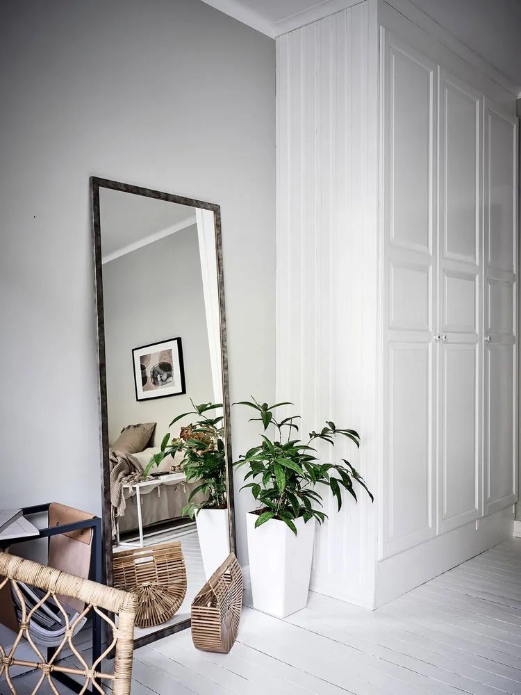 A modern minimalist living room with white flooring, wood furniture, and a tall floor mirror.