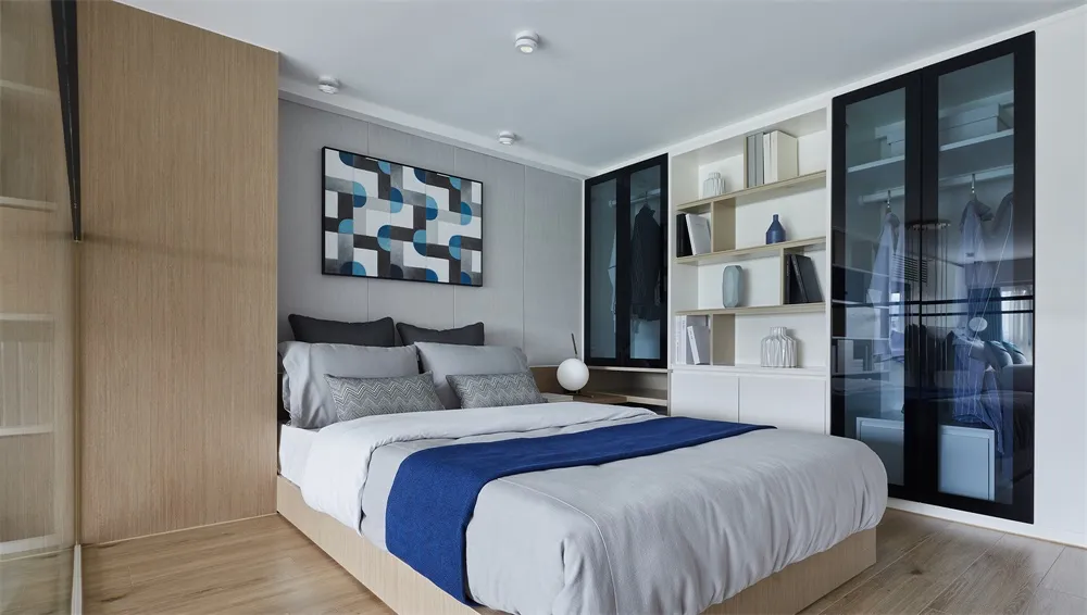 Modern bedroom with white walls and bed, featuring a blue and white geometric artwork on the wall.