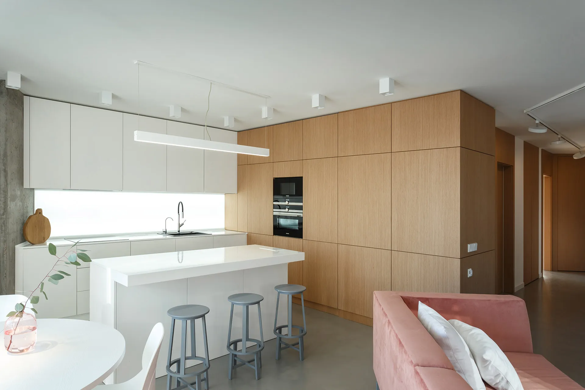 Modern minimalist kitchen with white laminate countertops, wood cabinets, and a bar counter with stools.