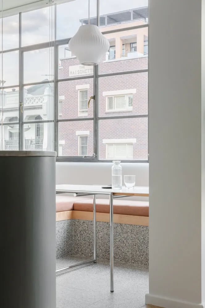 Modern cafe interior featuring a white cushioned seating area with a white table and vase, set against a backdrop of a glass 