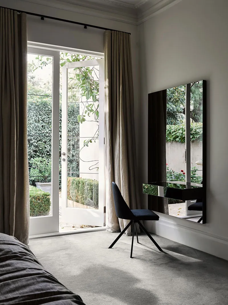 Minimalist bedroom featuring a metallic chair, glass mirror, and fabric curtains.