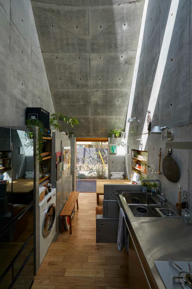 Modern minimalist kitchen with a concrete ceiling and floor, featuring a sink, stove, and washing machine