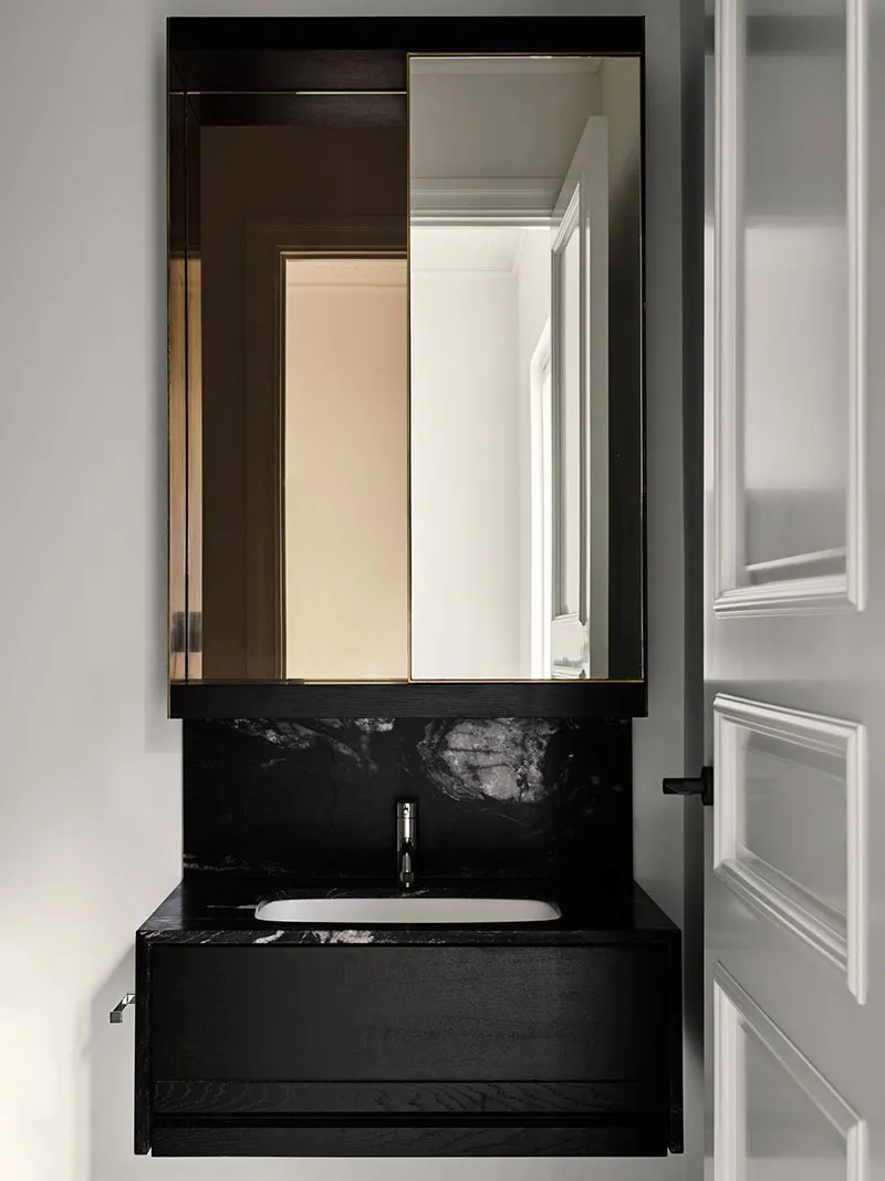 Modern bathroom with black marble sink and vanity, framed by a large rectangular mirror with a black wooden frame.