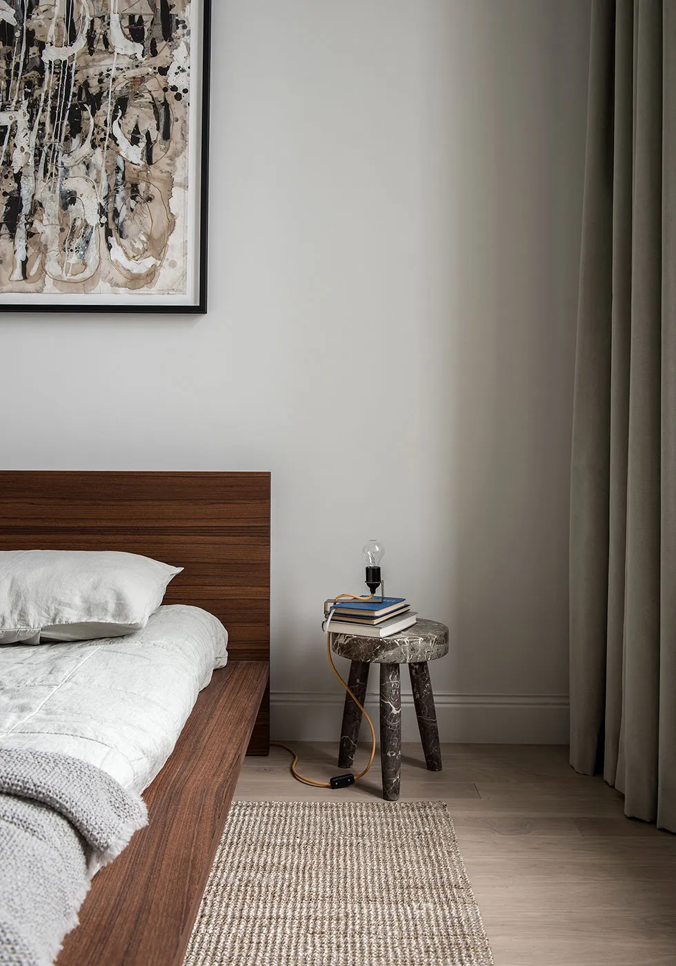 A modern minimalist bedroom featuring wooden furniture, marble accents, and a fabric bedspread.