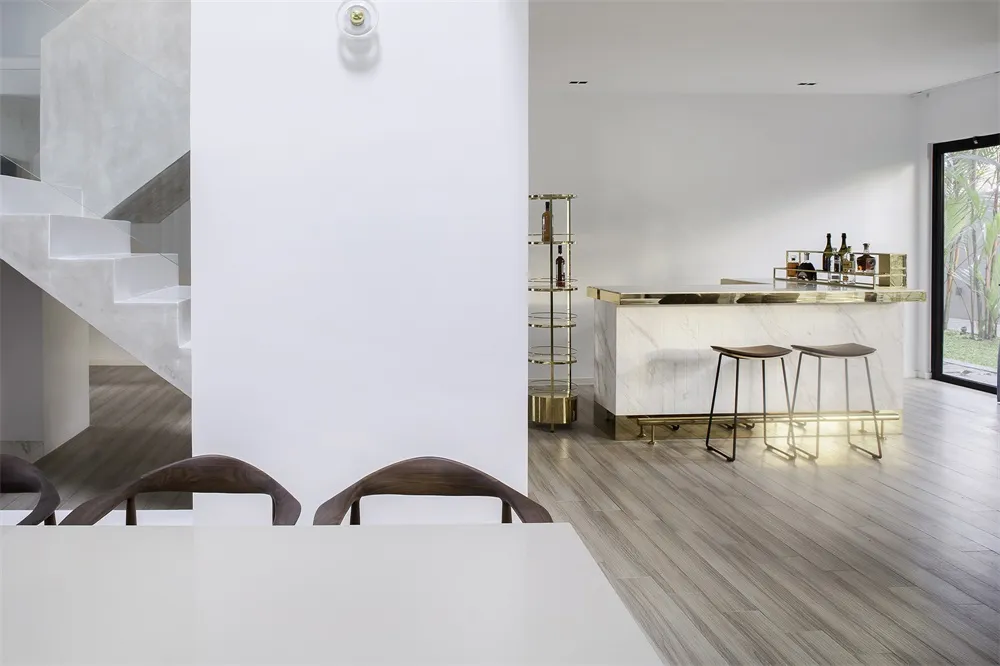 A modern minimalist dining room featuring concrete and marble materials, with a white dining table and wooden chairs.