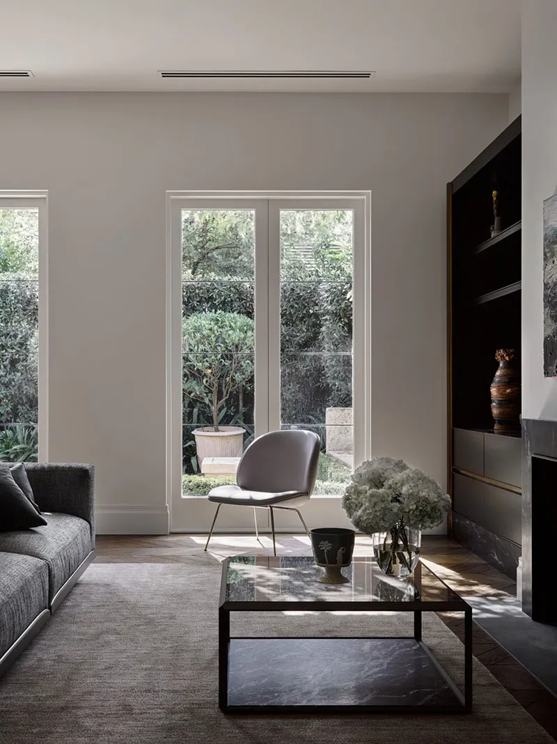 A modern minimalist living room featuring a glass and metal coffee table, a dark-colored sofa with a textured fabric, and a g