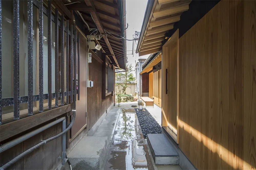A narrow street lined with wooden buildings, reflecting light and water puddles.