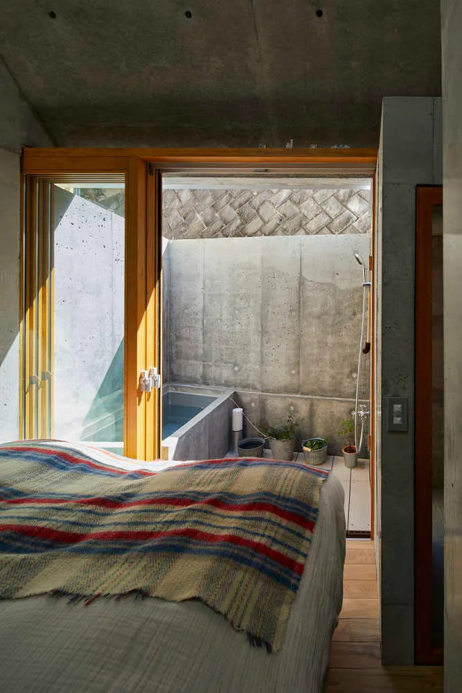 A minimalist bedroom with a concrete wall and wooden floor, featuring a bed with a striped blanket.