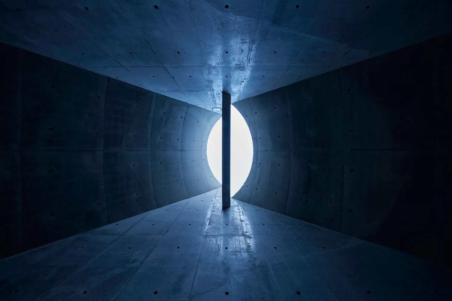 An industrial-style interior view featuring a minimalist design with concrete walls and a large circular opening.