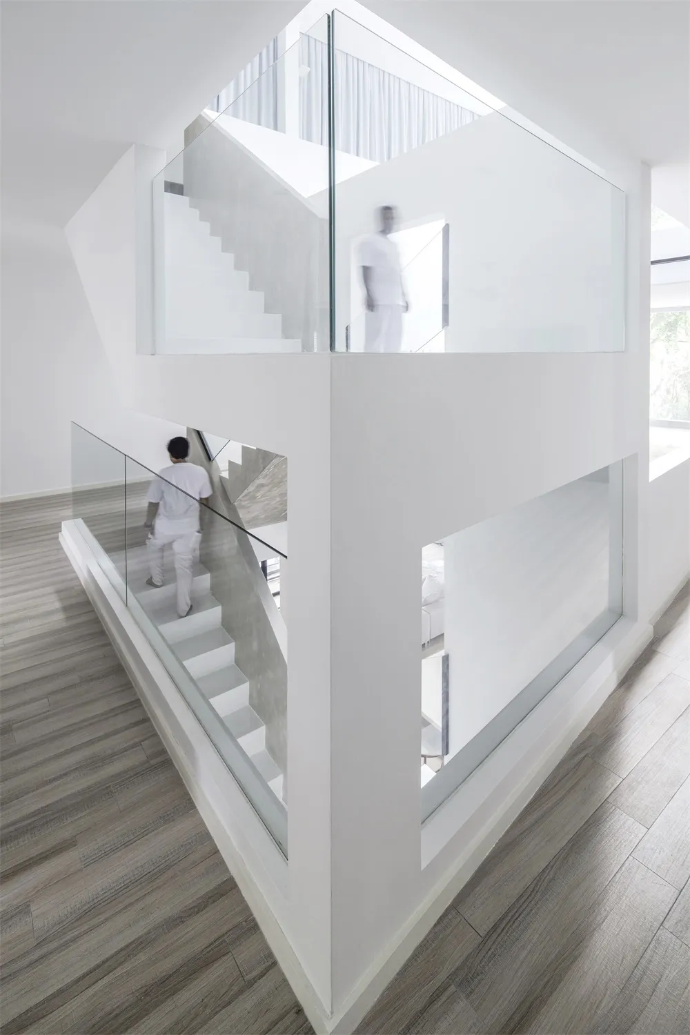 Minimalist, glass staircase interior with white walls and wooden flooring.