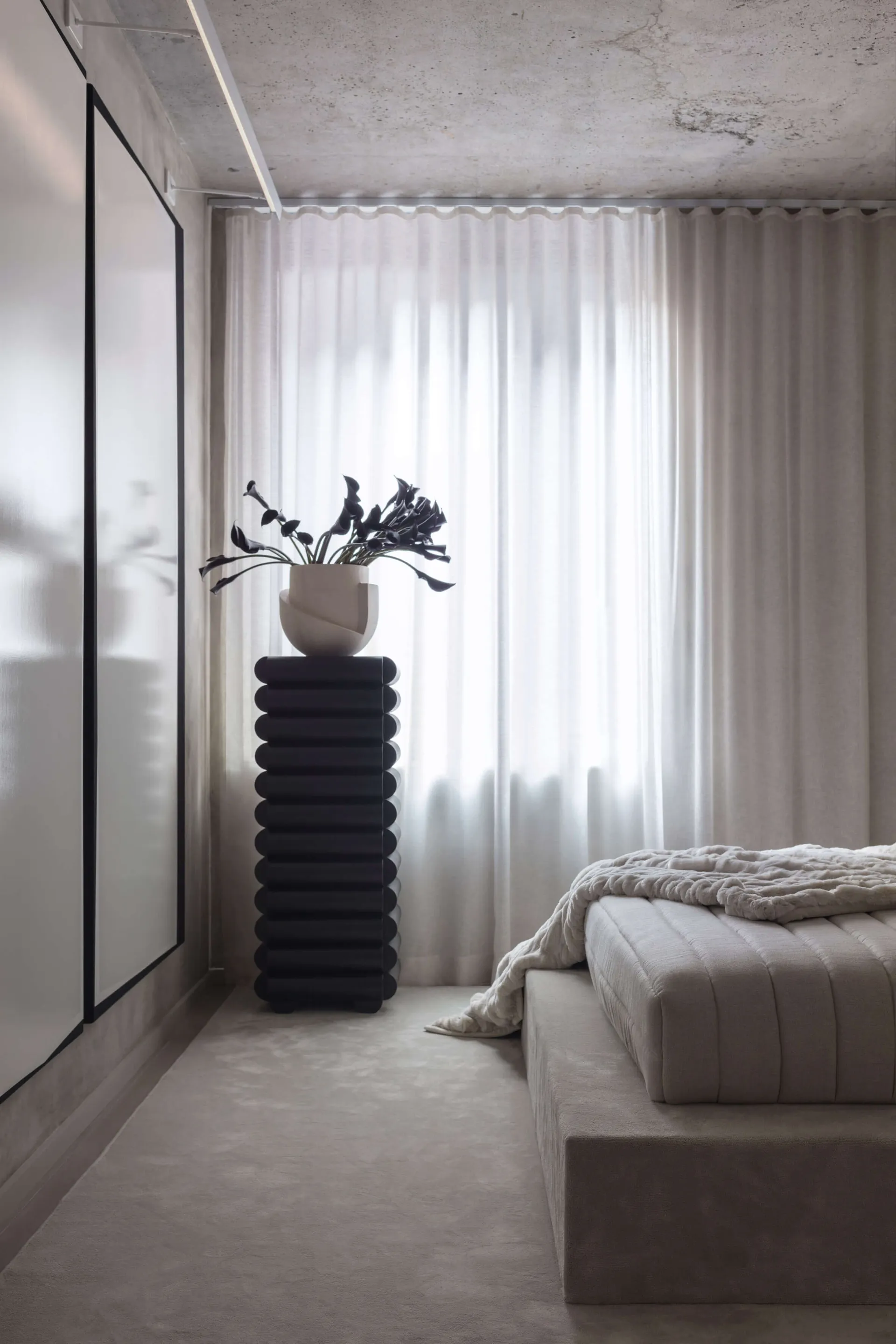 A minimalist bedroom featuring a textured sofa and textured elements, with white curtains and a concrete ceiling.