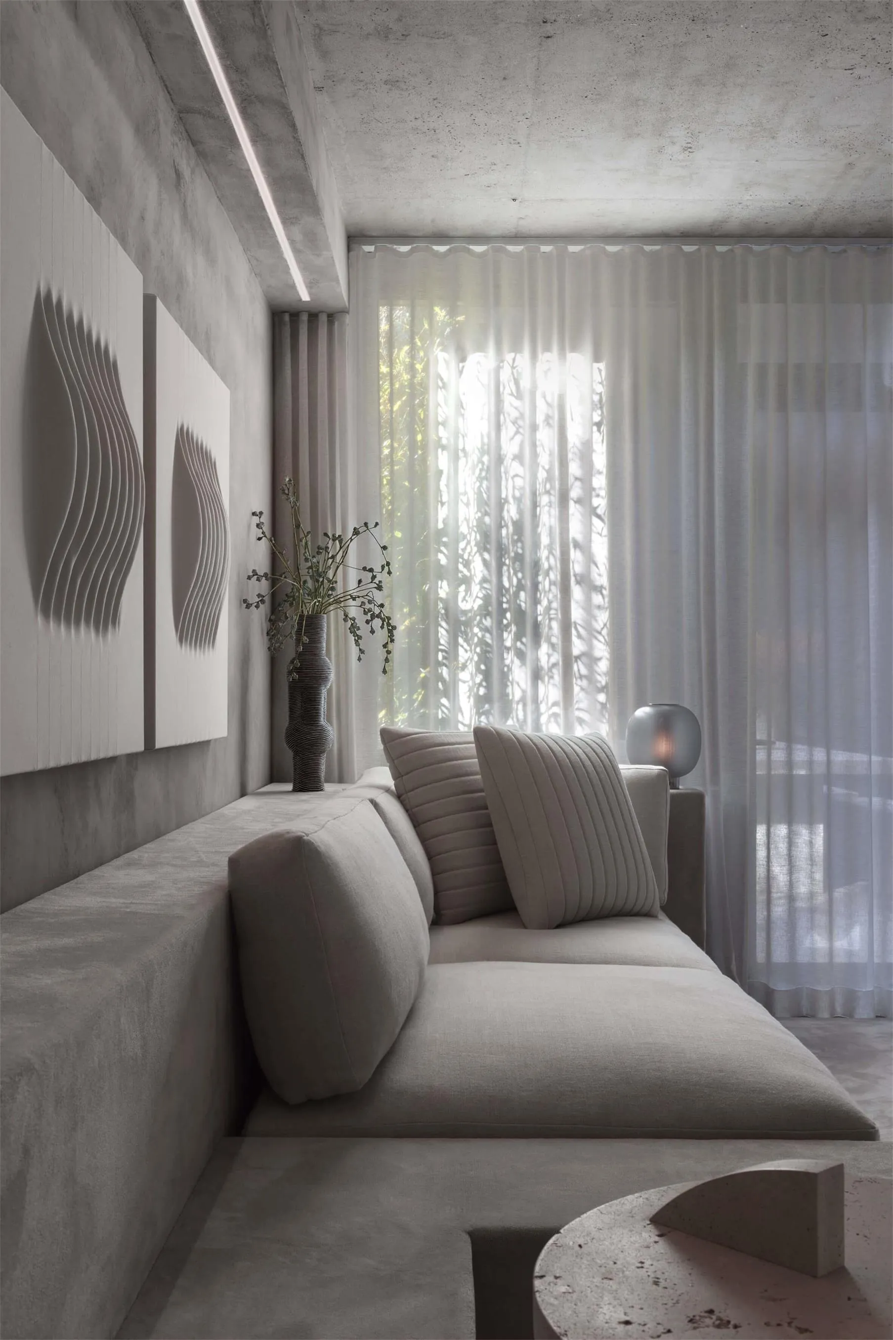 A modern minimalist interior with concrete walls, a gray sofa, and sheer curtains.