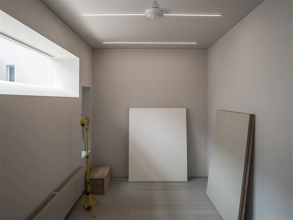A minimalist white interior space with white walls, floor, and ceiling, featuring natural light from a window and two large w