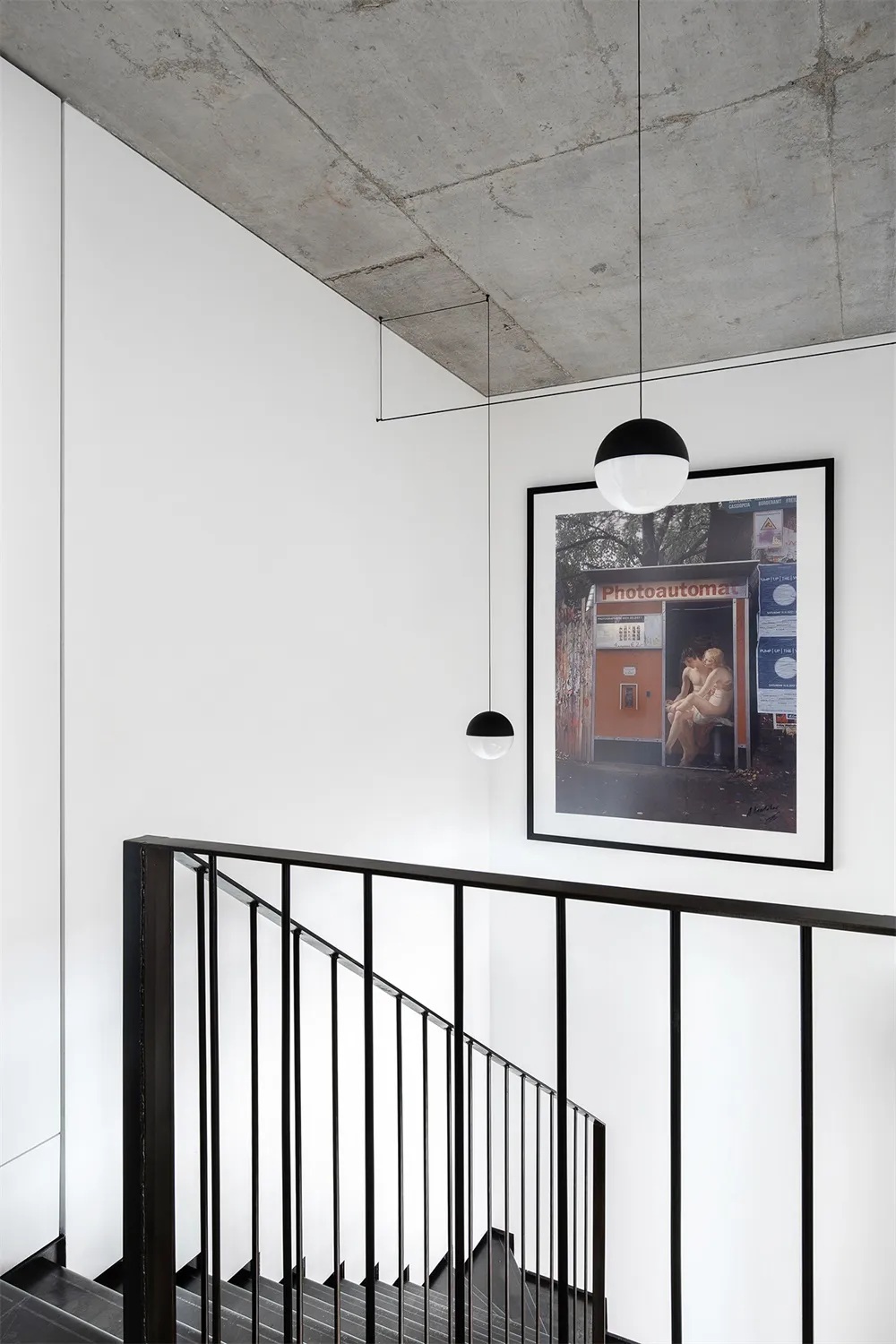 A minimalist industrial staircase with concrete walls and black metal railings, featuring a framed photograph of people in a