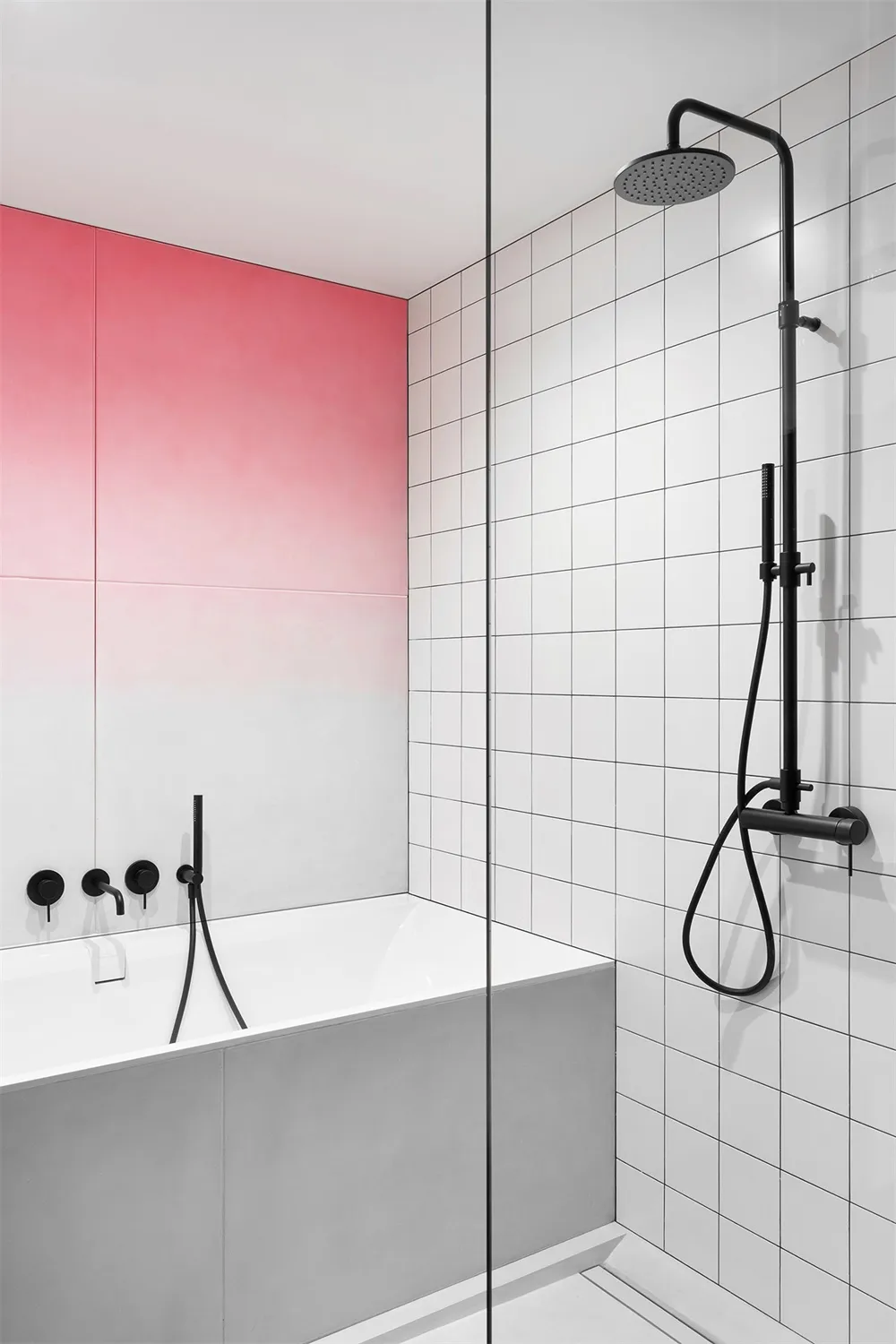 Minimalist bathroom with white, grey, and pink tiles, a concrete bathtub, and black fixtures.