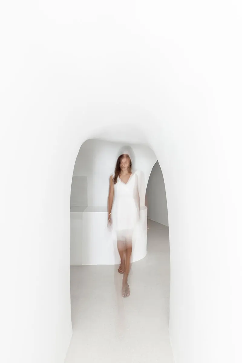 Blurred female figure in a minimalist, all-white environment