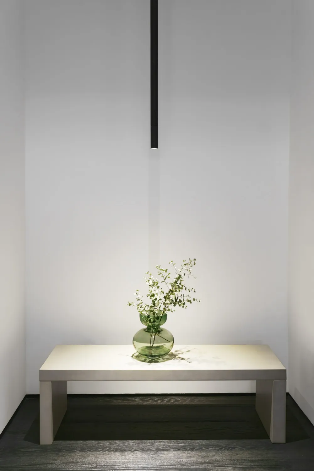 A minimalist interior design featuring a glass vase with greenery on a white table against a white backdrop.